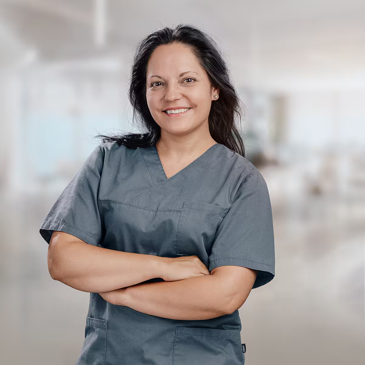 Dr. Diana Sannwald in grauer medizinischer Arbeitskleidung vor unscharfem neutralem Hintergrund.